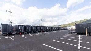 Un parking où sont alignées des rangées de conteneurs maritimes, et où se trouve un grand camion.