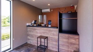 Une chambre d’hôtel moderne avec un plancher en bois, un petit tabouret en bois, un bureau intégré doté d’un ordinateur et d’un téléphone, et une grande fenêtre donnant sur un paysage verdoyant.