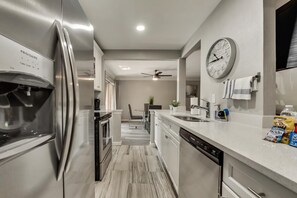 A modern kitchen with a stainless steel refrigerator, a dishwasher, and a clock on the wall. - GP54C - Upgraded 2BD Unit | Patio G. Prairie (Grand Prairie)