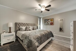 A bedroom with a tufted headboard, a patterned bedspread, a nightstand with a lamp, a dresser, and a ceiling fan. - GP54C - Upgraded 2BD Unit | Patio G. Prairie (Grand Prairie)
