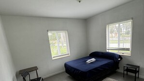 A bedroom with a bed, two windows, a chair, and a small table. - Villa by Eco-shared (Miami)