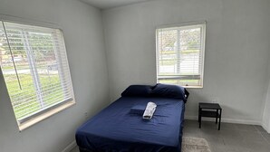 A bedroom with a bed, two windows, a small table, and a rug. - Villa by Eco-shared (Miami)