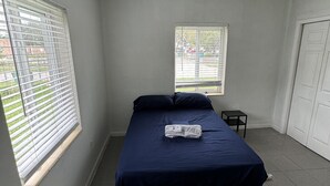 A bedroom with a bed, a small table, and a window with blinds. - Villa by Eco-shared (Miami)