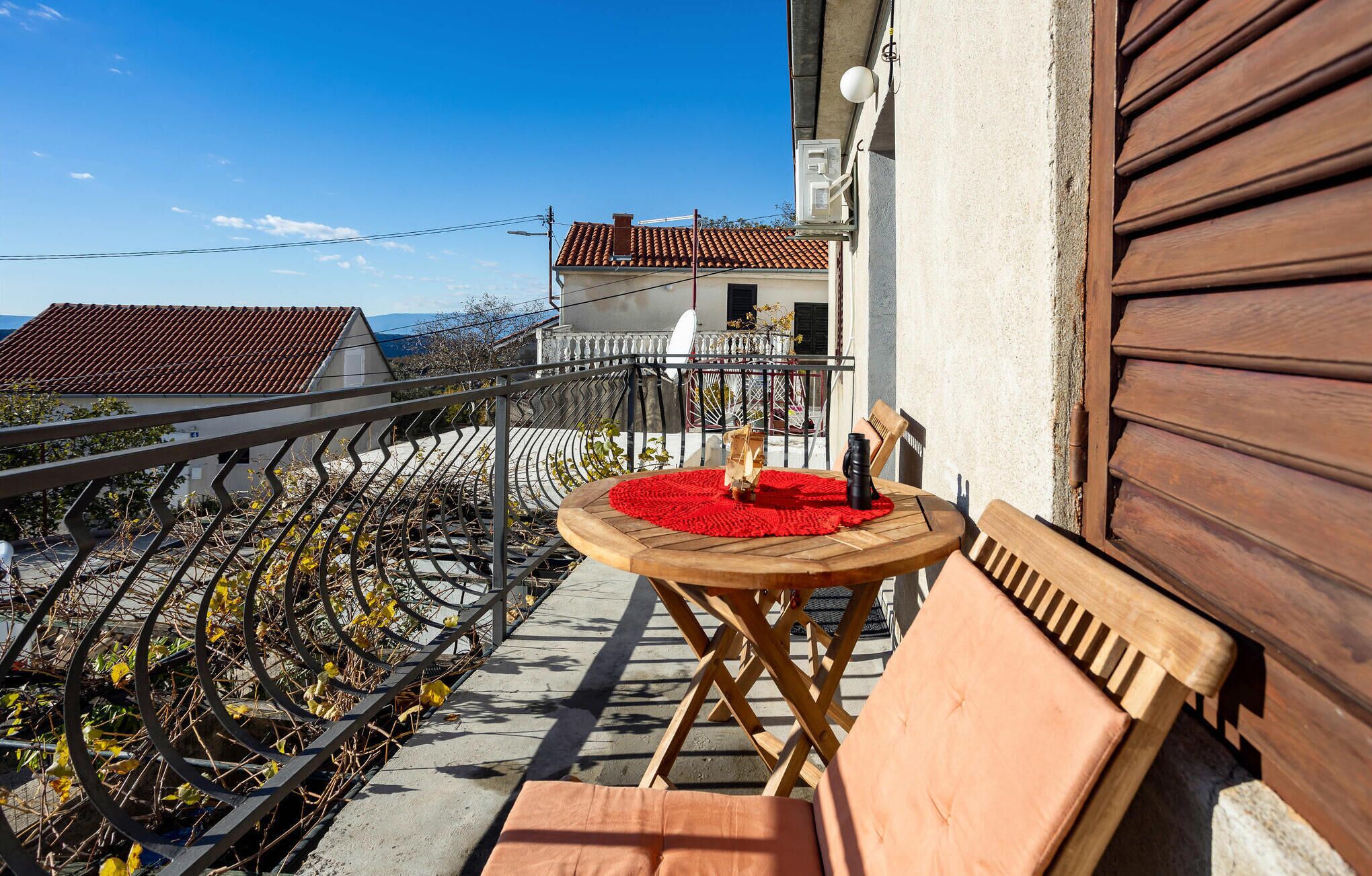 En balkon med en træstol og et bord, en rød måtte og en flaske.