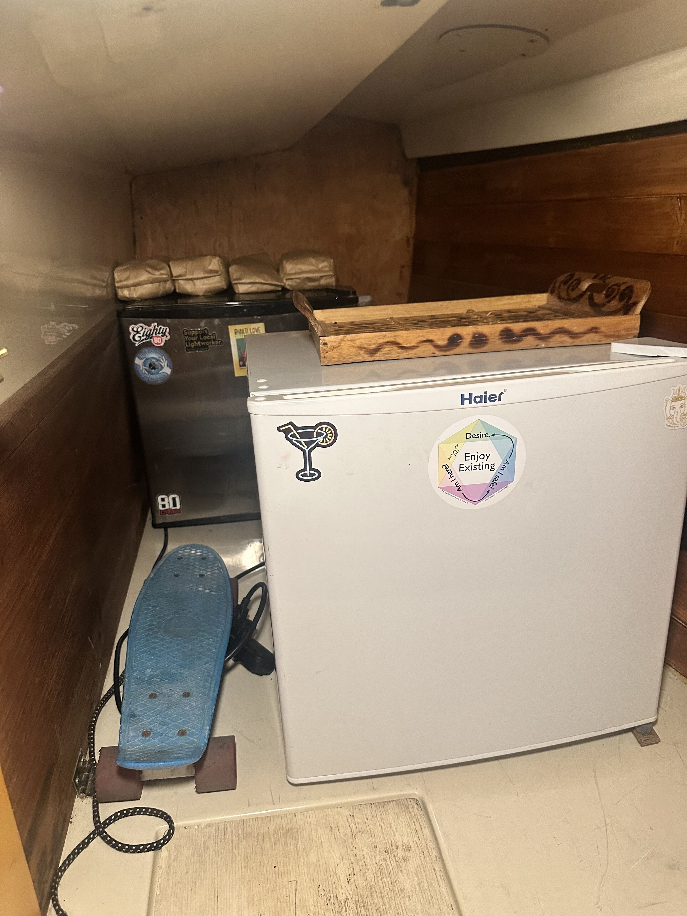 A compact kitchen area with a refrigerator, a small freezer, and a wooden shelf.