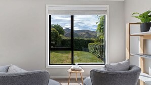 Habitación con un ventanal grande que ofrece vistas a un jardín y montañas. Hay dos sillones grises y una mesita con una caja de pañuelos.