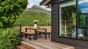 Terraza de madera con una mesa y bancos, con vistas a un paisaje montañoso.