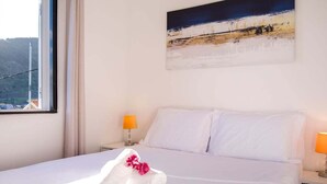 A hotel room with a bed, two bedside lamps, a window, and a painting on the wall. - GuestReady - Machico sea view residence - A (Machico)