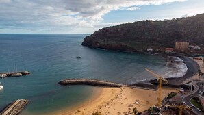 A coastal area with a sandy beach, a rocky cliff, and a pier. - GuestReady - Machico sea view residence - A (Machico)