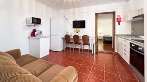 A compact living space with a kitchenette, a dining area with chairs, a sofa, and a TV mounted on the wall. - GuestReady - Machico sea view residence - A (Machico)