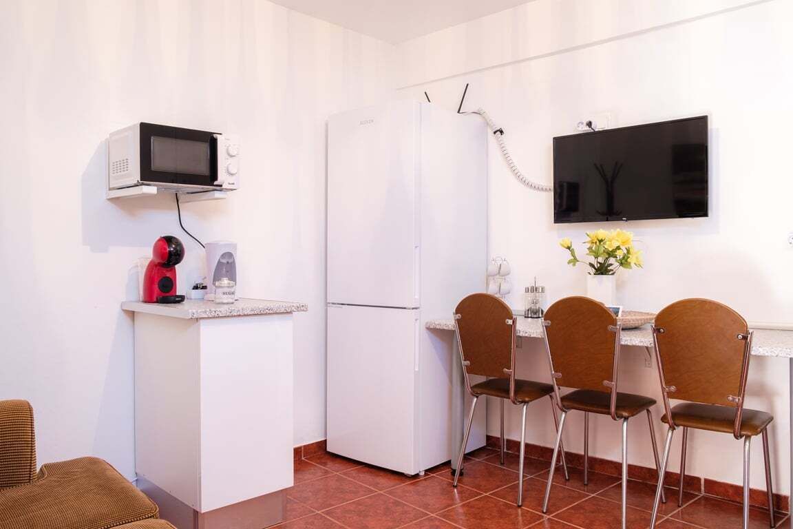 A compact kitchen with a microwave, refrigerator, and a flat-screen TV mounted on the wall.