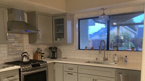 Eine moderne Küche mit weißen Schränken, Edelstahlgeräten und einem großen Fenster mit Blick ins Freie.