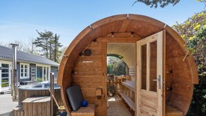 Una estructura cilíndrica de madera con un banco y una mesa pequeña, una puerta abierta y una vista de un edificio al fondo.