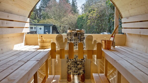 Una sauna con bancos de madera y techo de vidrio, con vistas a árboles y un edificio al fondo.