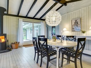 Een eetgedeelte met een ronde tafel, zwarte stoelen met witte stippen, een hanglamp, een open haard en een groot raam met uitzicht op groen.