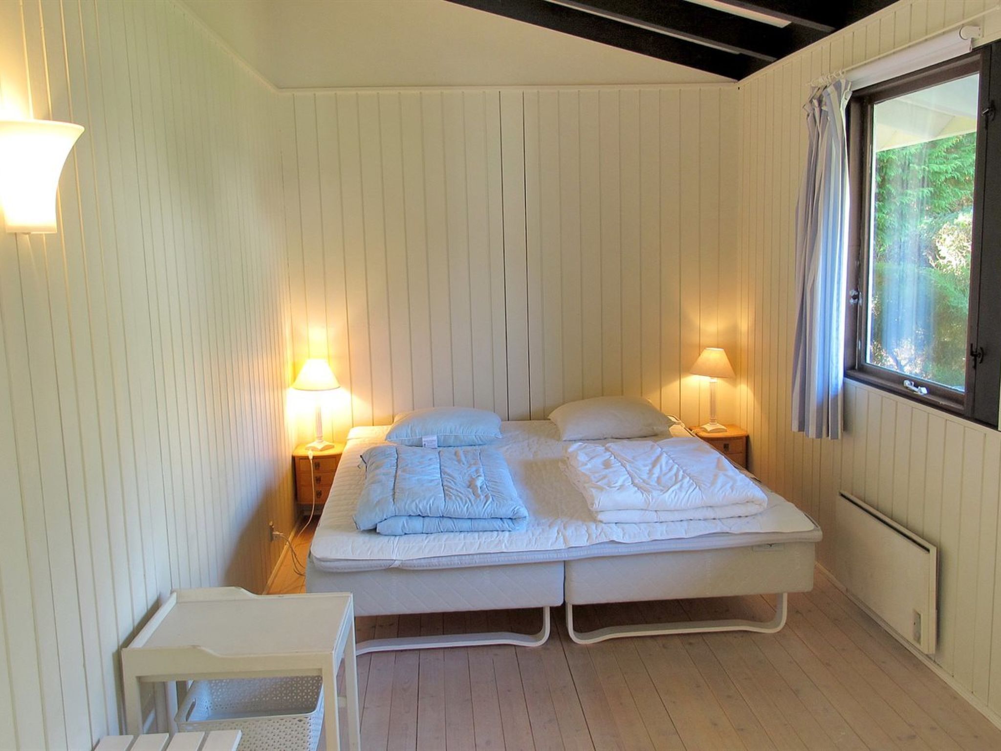 A double bed with two pillows, bedside lamps, a small table, and a window with curtains.