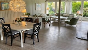 Een eetruimte met een ronde tafel en stoelen, een kroonluchter en uitzicht op het buitenlandschap door grote ramen.