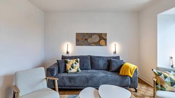 A modern living room with a grey sofa, two armchairs, a coffee table, and a geometric artwork on the wall.