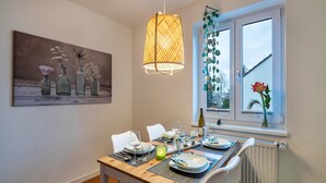A dining area with a table set for four, a hanging light fixture, a window with a view, and a painting on the wall. - Apartment 'Apartement Hangarstein' with Balcony and Wi-Fi (Kassel)