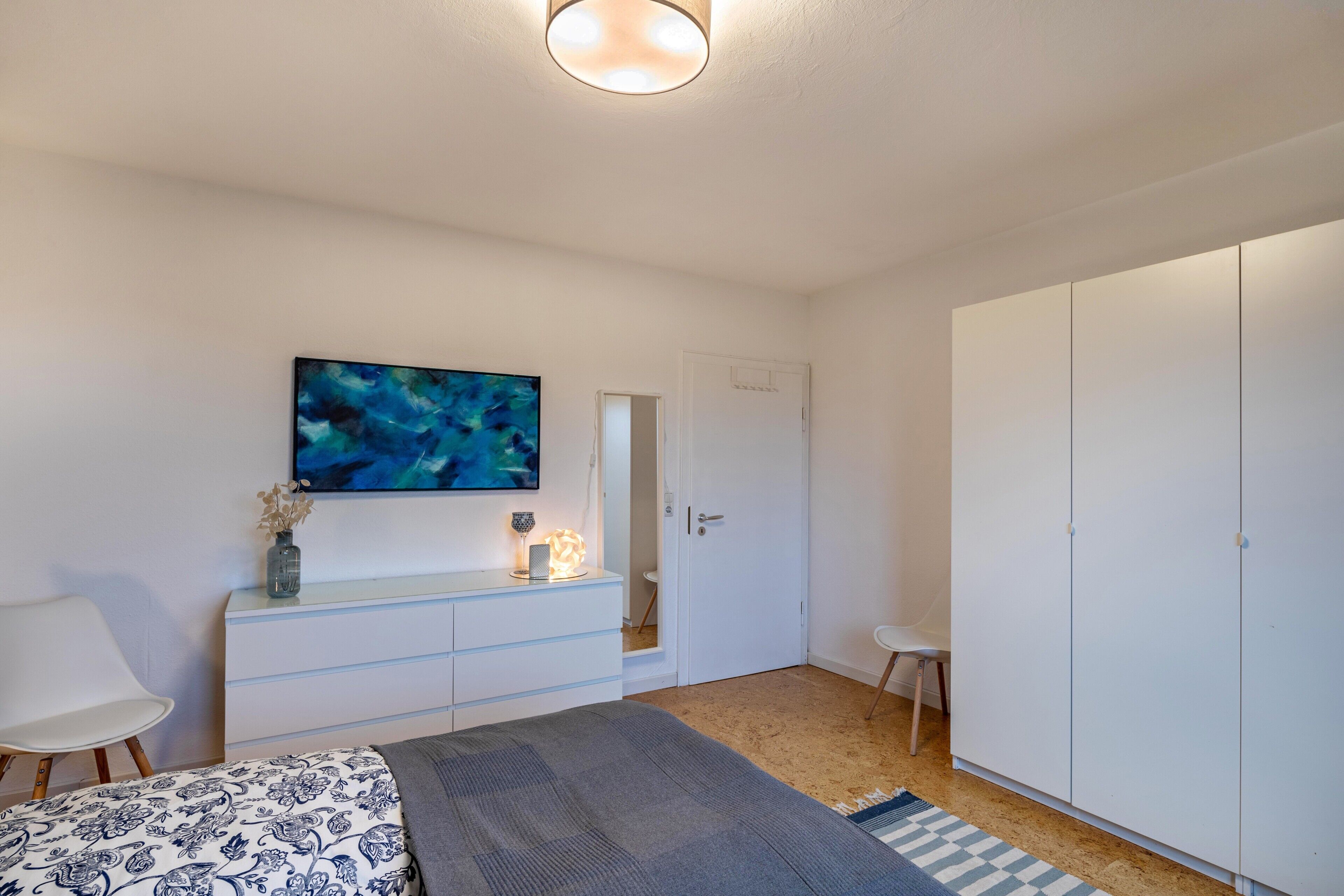 A bedroom with a bed, a dresser, a TV, a wardrobe, and a door leading to another room.