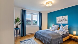 A bedroom with a bed, a window with curtains, a radiator, a potted plant, and a wall-mounted light fixture. - Apartment 'Apartement Hangarstein' with Balcony and Wi-Fi (Kassel)