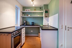 A compact kitchen with a stove, oven, and countertop. There are shelves above the counter and a door to the right.