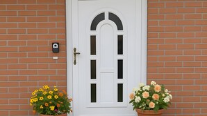A white door with a small porch area, two potted plants, and a brick wall. - "Kijas" holiday flat with private terrace and WLAN (Wismar)