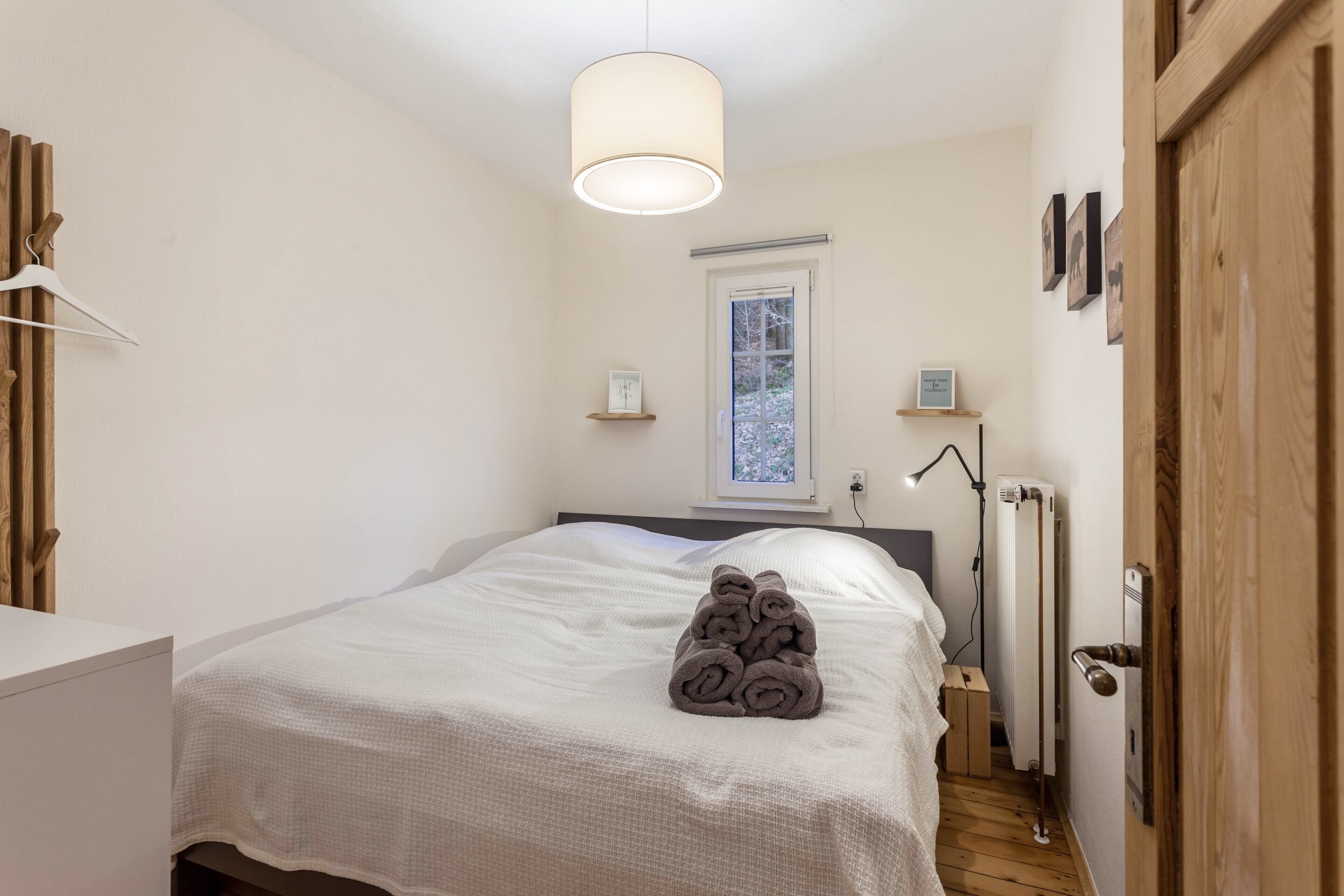 A bedroom with a bed, a hanging light fixture, a radiator, and a window.