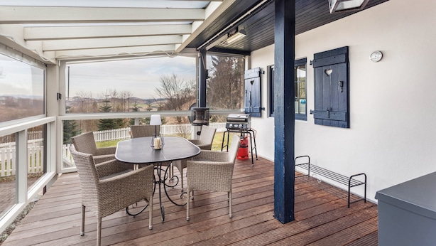 Een terras buiten met een tafel, stoelen, een barbecue en uitzicht op het landschap.