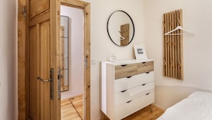 Een kamer met een houten deur, een witte kapstok met lades, een ronde spiegel, een houten wandpaneel en een witte kleerhanger.