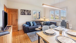 Een moderne woonkamer met een bank, een eettafel voor vier personen, een televisie en kunst aan de muur.