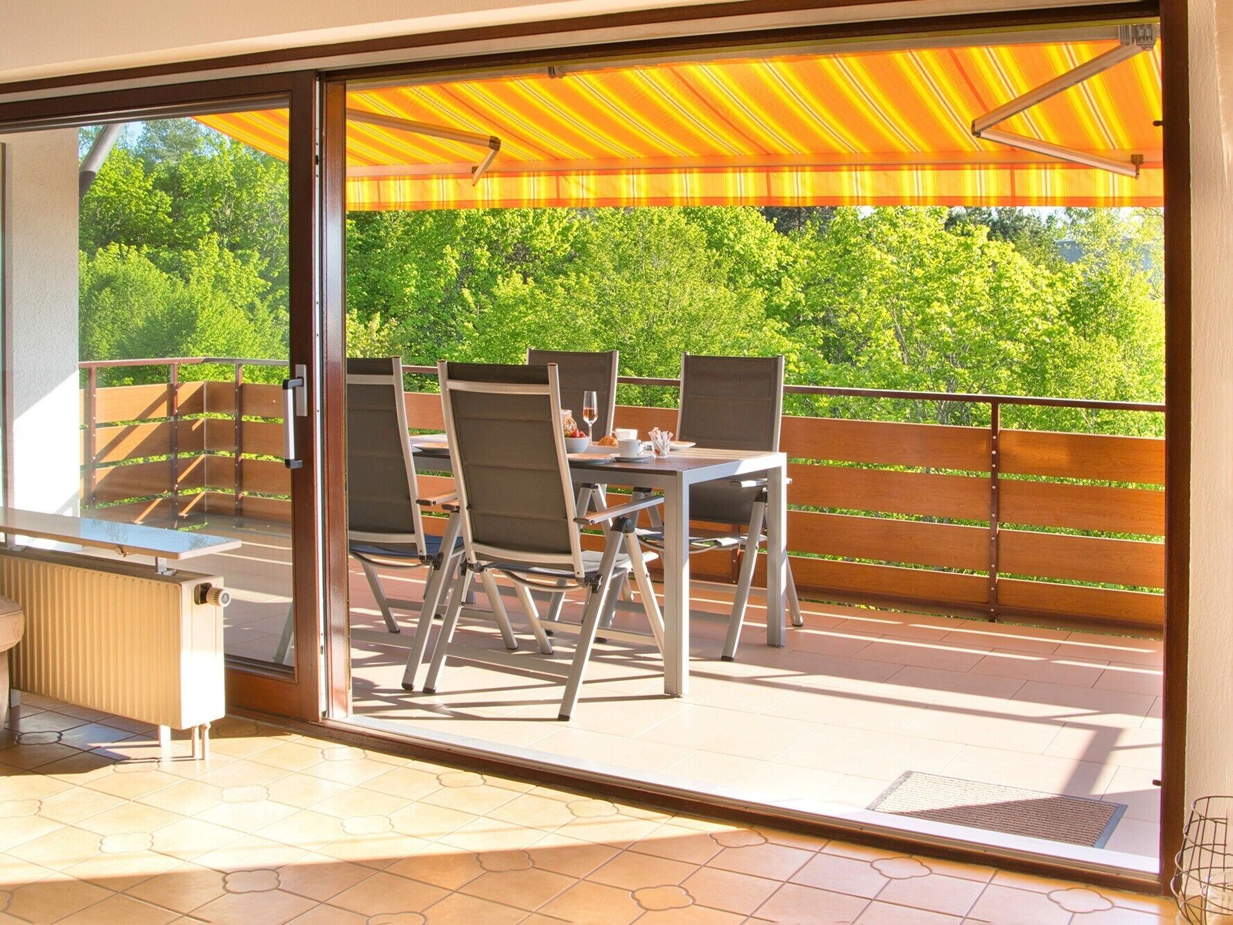 Un balcon avec une table et des chaises, une porte vitrée et une vue sur la verdure.