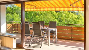 A balcony with a table and chairs, a glass door, and a view of greenery. - Apartment 'Seerose' with Shared Garden, Balcony and Wi-Fi (Überlingen)