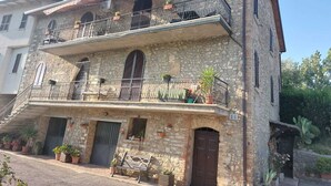 A two-story stone building with balconies, a wooden bench, and potted plants. - L'Antica Sosta (Corciano)