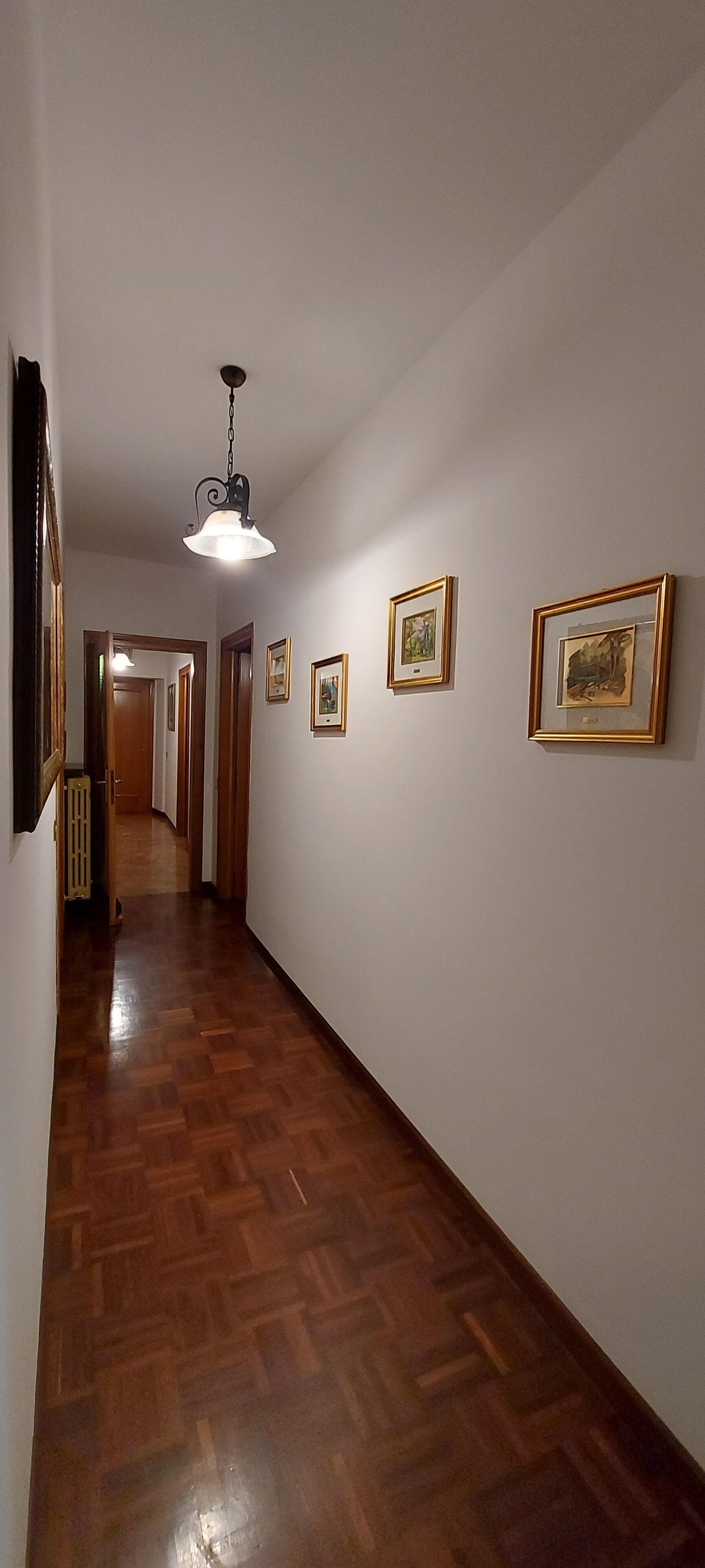 En hall med trägolv, inramade tavlor på väggarna och en hängande lampa.