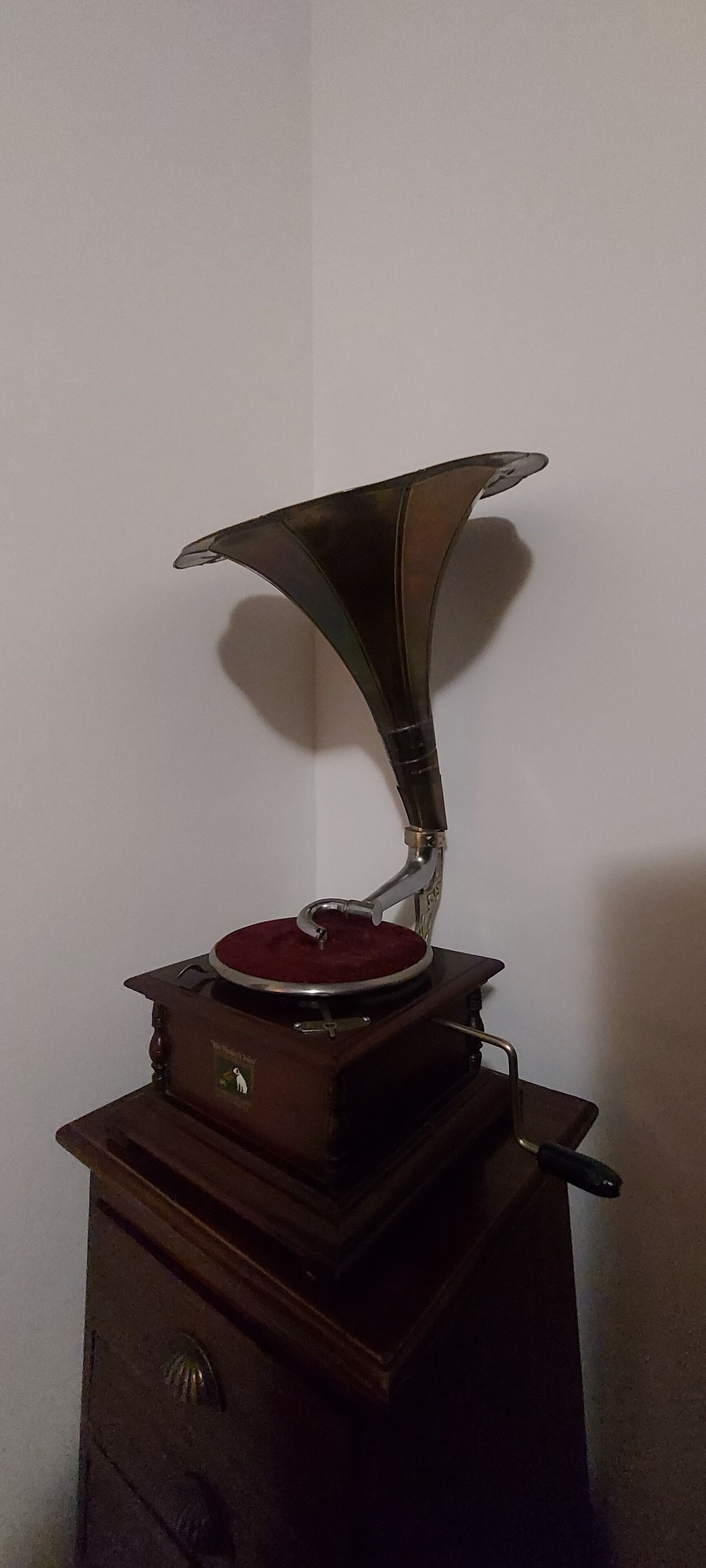 Un gramófono antiguo sobre un mueble de madera frente a una pared lisa.