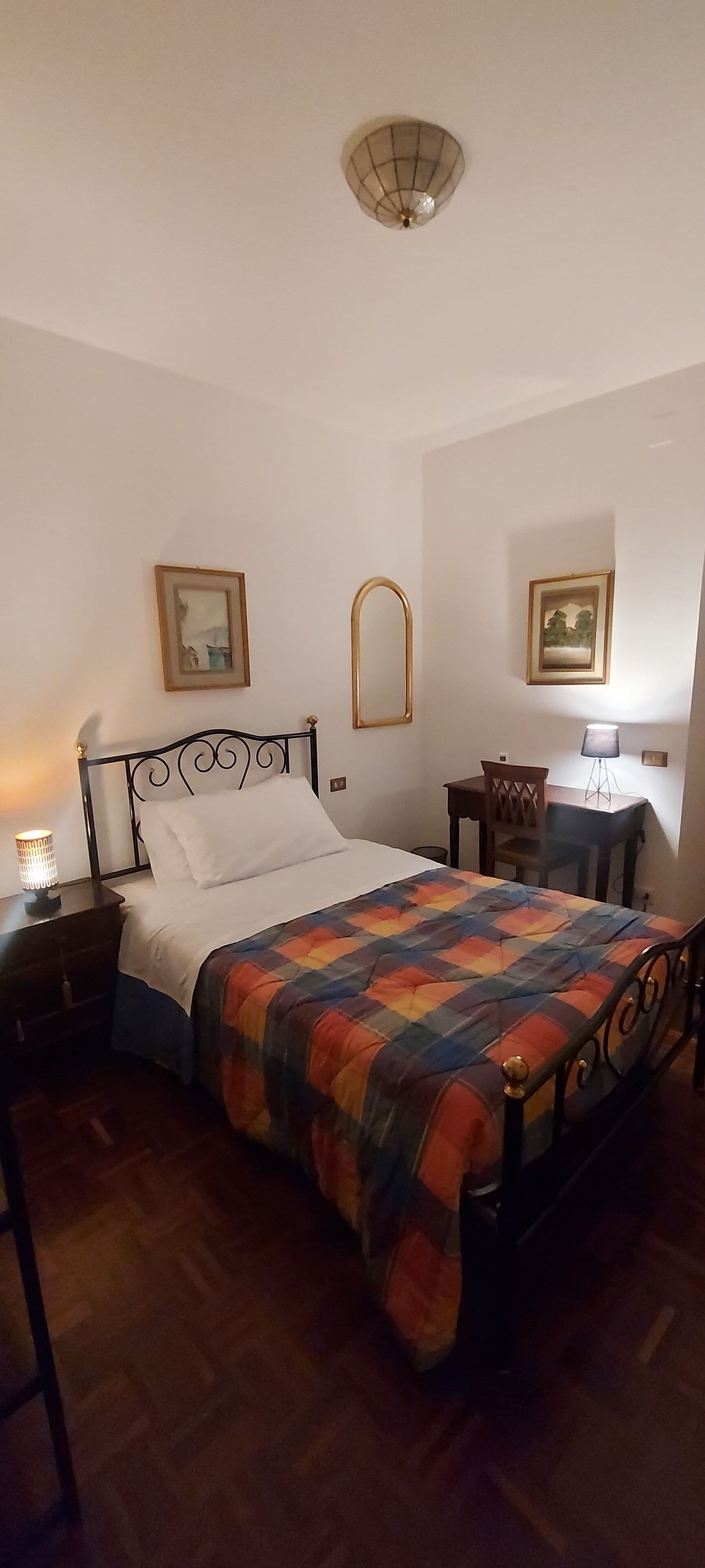 A bedroom with a bed, a nightstand, a desk, a chair, and a lamp.