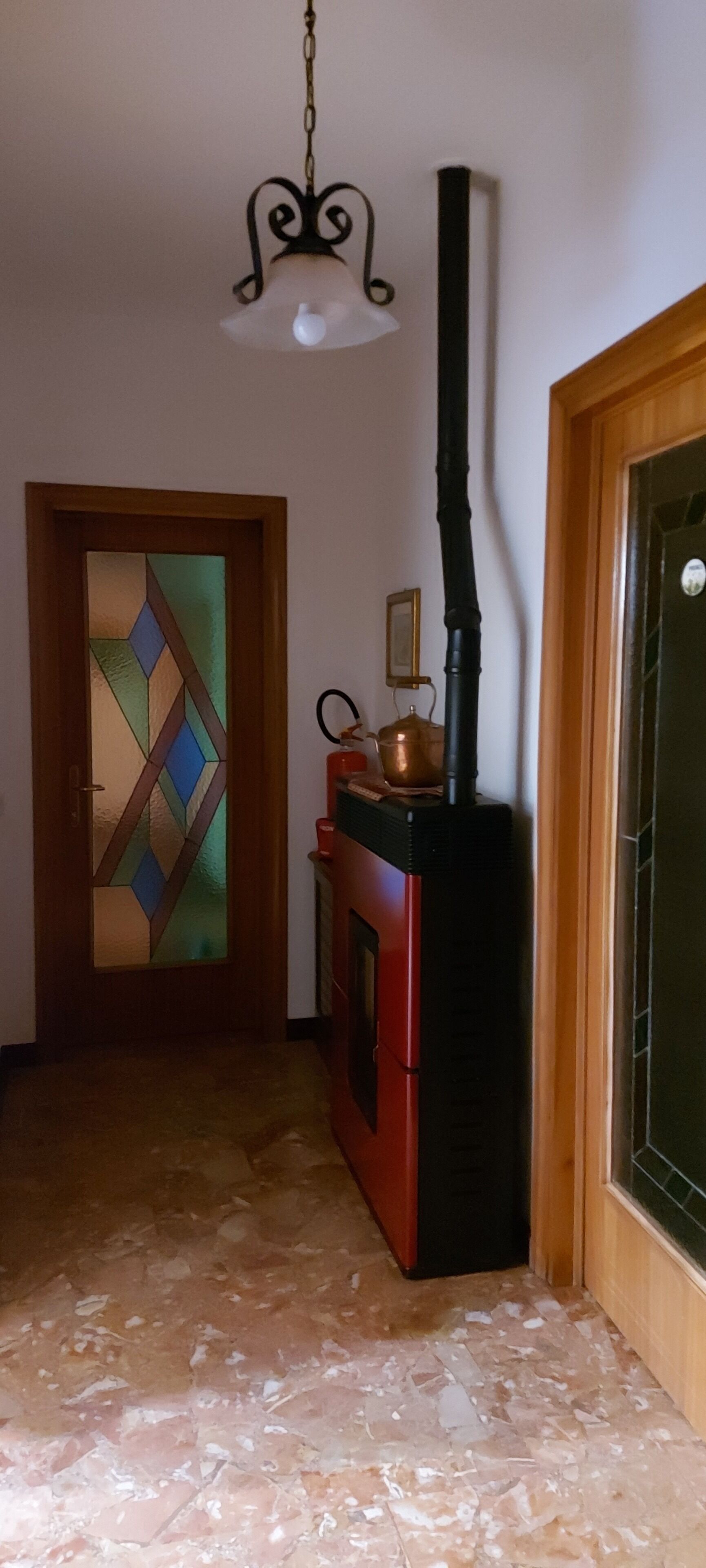 A hallway with a wooden door, a red stove, and a black chimney.