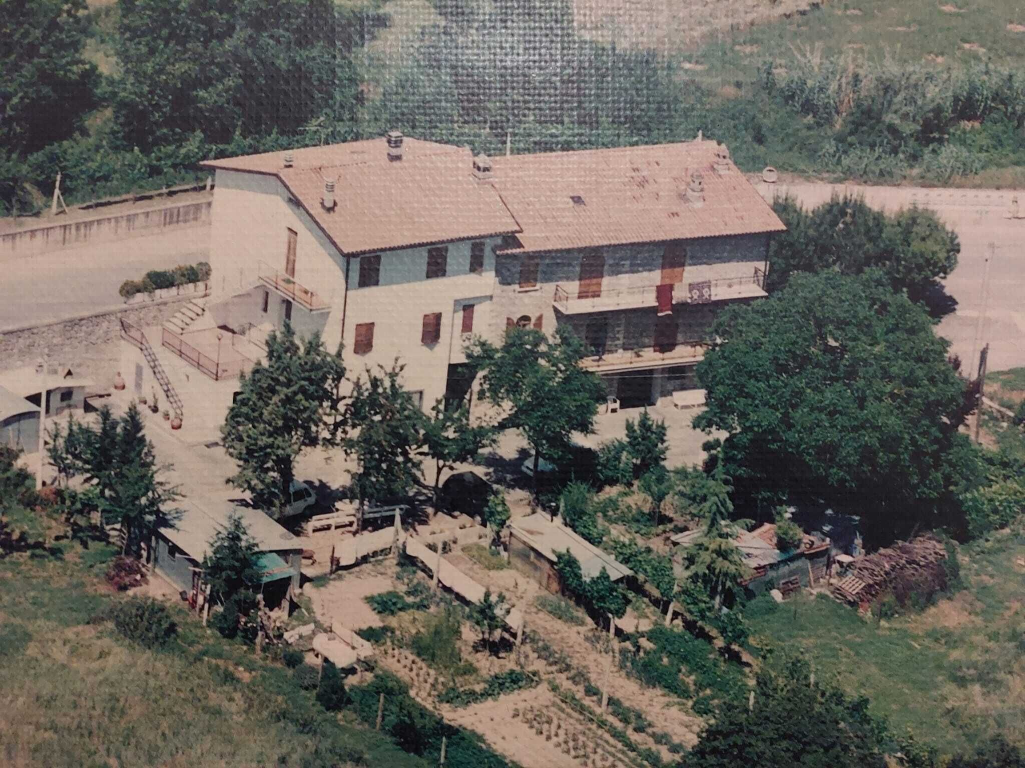 A two-story building with a flat roof, surrounded by trees and a garden.