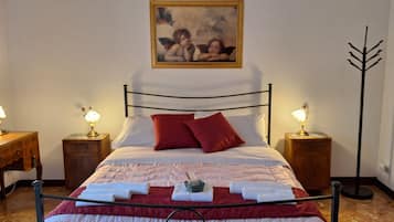 Un lit bien fait, avec du linge de lit rouge et blanc, deux tables de chevet avec des lampes, un bureau en bois et un tableau accroché au mur.