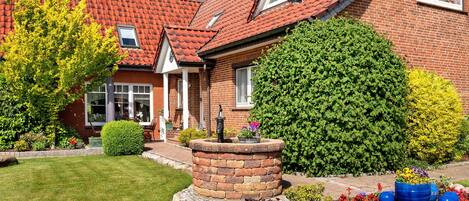 A brick house with a red-tiled roof, a well-maintained lawn, and a flower bed with various plants.
