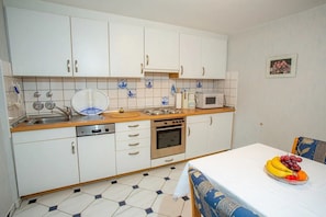 A compact kitchen with white cabinets, a microwave, a stove, and a sink. There's a dining table with a fruit bowl on it.