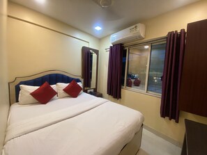 Ein Hotelzimmer mit Bett, Nachttisch, Spiegel, Klimaanlage, einem Vorhangfenster und Blick auf die beleuchtete Stadt.
