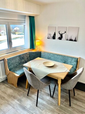 Un coin salon avec une table, des chaises, une lampe et des œuvres d’art accrochées au mur.