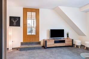 A modern living room with a wooden door, a flat-screen TV, a staircase, and a glass table. - 4 Ferienwohnung Maiglöckchen, 35qm mit 1 Schlafzimmer für max. 4 Personen (Höchenschwand)