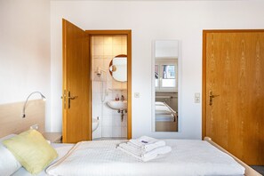 A hotel room with a bed, a bedside table, a lamp, a mirror, a bathroom with a sink and toilet, and wooden doors.