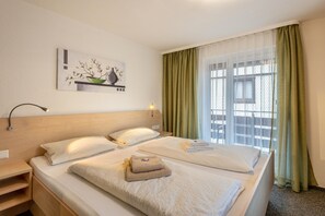 Une chambre d’hôtel avec un lit, une table de chevet, une lampe, un tableau et une fenêtre avec des rideaux.