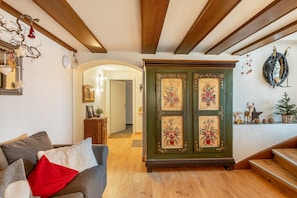 Un salon comprenant un canapé, un meuble en bois orné de motifs floraux, un escalier et un porte-manteau fixé au mur.