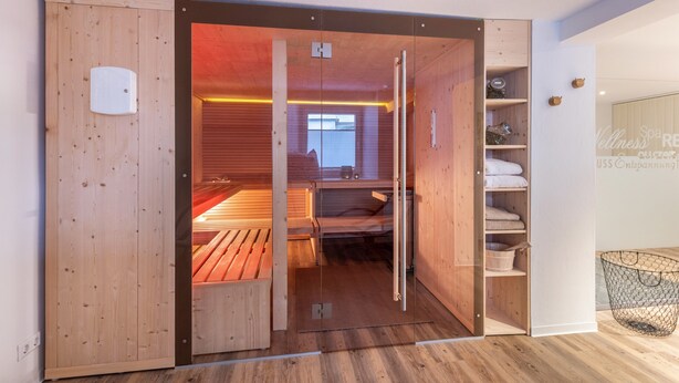 Un sauna avec des bancs en bois, une porte en verre et une étagère où sont rangées les serviettes.