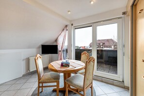 A room with a round table, two chairs, a flat-screen TV, a radiator, and a sliding glass door leading to an outdoor area.